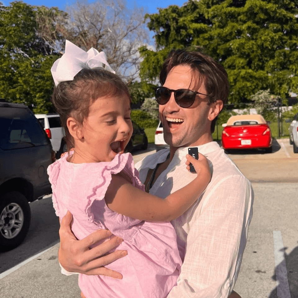 Jason Colapietro smiling while holding a child outdoors.
